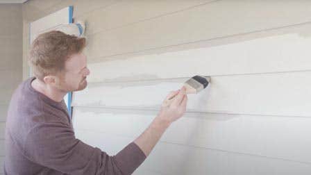 A person painting a weatherboard home